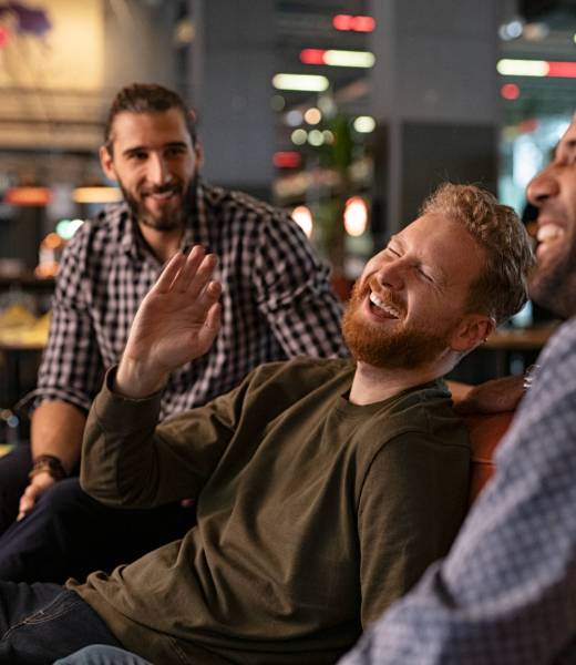 Mid adult men friends enjoying at pub Group of three best friends laughing and enjoying the evening at pub. Happy young men enjoying late night staying together at bar. Cheerful guys sitting on couch and having fun while relaxing after work.